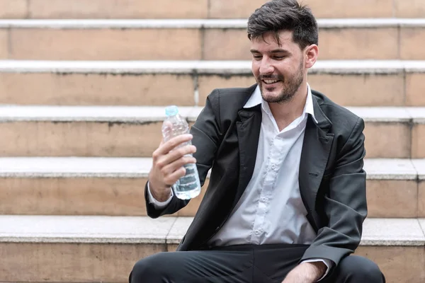 Tired sale man concept. Tired direct sale man resting and drinking water after a hard day of work. Taken outdoor, business team spirit, and refreshing ideas concepts.