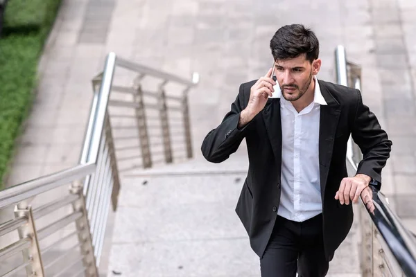 Mobile office concept.  Handsome successful white business man or sale man talking on his cell phone while walking up stairs. Taken outdoor, apply urban looks effect.