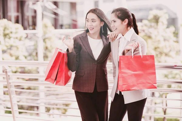 Two beautiful girls shopping together. Asian woman and white girl smartly dress going out shopping during lunch time in work days. Taken outdoor with natural lights in business district walk way.