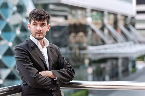 Confident young business man portrait concept. Handsome white male in black suit, black hair and beard taken outdoor with natural light, successful modern business man concept.