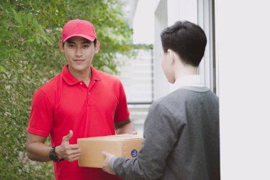 Genç lojistik kariyer kavramı. Mutlu teslimatçı onun paketi evde müşteriye verilmesi. Gerçek evde çekilmiş. Onun erken yirmili kırmızı şapkalı adam kırmızı polo tişört ve kot Asya Çin uygun.