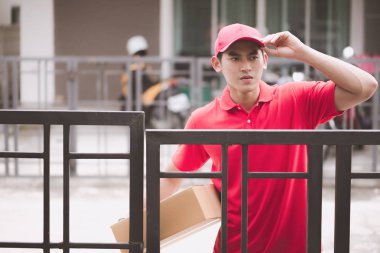 Genç lojistik kariyer kavramı. Onun müşterilerinin evlerine arayan mutlu teslimat adam. Gerçek evde çekilmiş. Onun erken yirmili kırmızı şapkalı adam kırmızı polo tişört ve kot Asya Çin uygun.