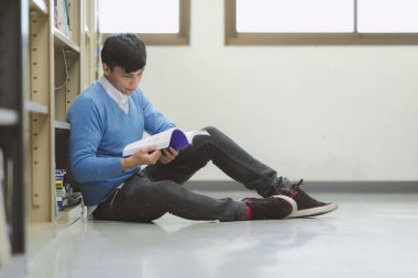 Kütüphane genç öğrenci çalışmada zor. Asyalı erkek üniversite öğrenci zemin ve odaklanarak kitap okuma kitaplığındaki çalışma araştırma yapıyor. Okul eğitim çeşitlilik kavramı için geri.