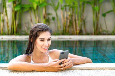 Güzel genç tek beyaz kadın havuzda. İstimal hareket eden telefon, beyaz bikini giyiyor. Bağlı dünya kavramı.