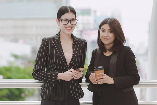 Two beautiful confident asian business woman taking a coffee break during break time. Two women in office suits talking during office break time, taken outdoor in natural light. Career woman concept.