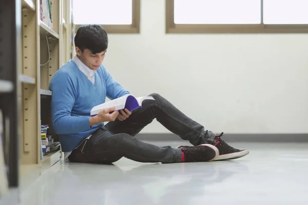 Young student study hard in library. Asian male university student doing study research in library reading book on floor and focusing. For back to school education diversity concept.