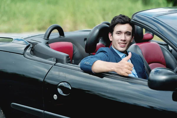 Holiday Car rent and road trip concept. Handsome white man inside a black convertible doing a thumps up pose with nature background, looking into camera, ready for a road trip and long drive.