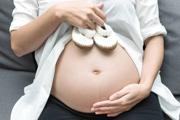 健康的中国母性观念 年轻的中国孕妇的画像在她的家和抱着婴儿鞋在她的肚子 采取室内与真正的六月大孕妇 — 图库照片