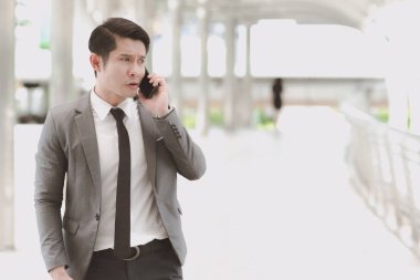 Kendine güvenen genç iş adamı akıllı ofis takım elbiseli. Gri ceket geçit arka planda telefonla konuşurken siyah saçlı yakışıklı Asya erkek işçi.