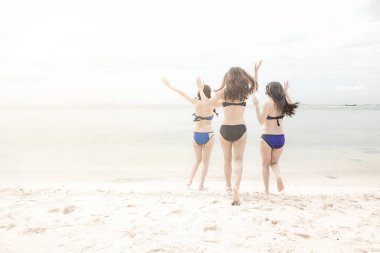 Grup güzel genç tek Çinli kadını kumsalda eğleniyor. Okyanusa doğru bikini, plaj şapka giyen deli çalıştıran.