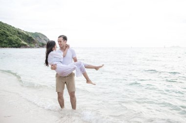 Birbirimizi kumsalda tutan bir çift. Birbirimizi tutan sahilde genç mutlu ırklararası çift. Asyalı kadın, beyaz adam. Genç karışık yarış romantizm kavramı.