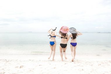 Grup güzel genç tek Çinli kadını kumsalda eğleniyor. Okyanusa doğru bikini, plaj şapka giyen deli çalıştıran.