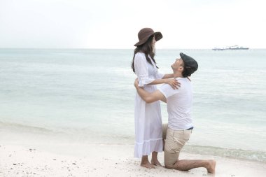 Adam sahilde kadın için teklif. Sahilde kız arkadaşı için teklif genç mutlu beyaz erkek dizlerinin üzerinde. Asyalı kadın, beyaz adam. Genç karışık yarış romantizm kavramı.