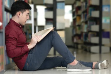 Kütüphane genç öğrenci çalışmada zor. Asyalı erkek üniversite öğrenci zemin ve odaklanarak kitap okuma kitaplığındaki çalışma araştırma yapıyor. Okul eğitim çeşitlilik kavramı için geri.