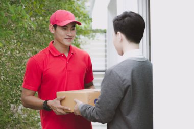 Genç lojistik kariyer kavramı. Mutlu teslimatçı onun paketi evde müşteriye verilmesi. Gerçek evde çekilmiş. Onun erken yirmili kırmızı şapkalı adam kırmızı polo tişört ve kot Asya Çin uygun.