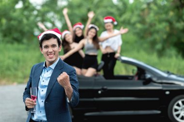 Noel playboy parti kavramı. Genç beyaz erkek stand yan tarafındaki üstü açık spor araba pembe şampanya dört güzel Asyalı kadınlar ile Noel Baba şapkası giyen arka planda tutan.