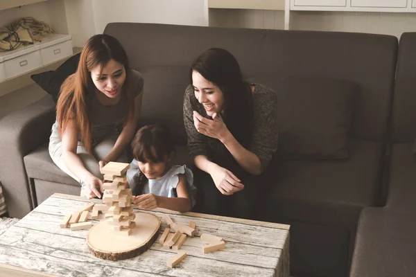 Two woman playing puzzle game with their daughter in living room. Family fun time concept.