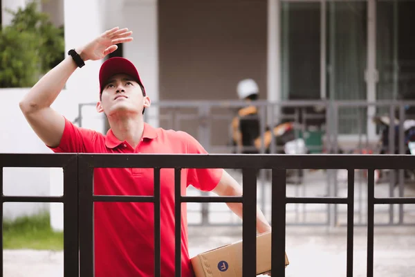 年轻的后勤职业概念 快乐的送货人在家里寻找他的顾客 在真正的房子 二十岁代初 亚洲华人身穿红色马球衫和红帽牛仔裤 — 图库照片