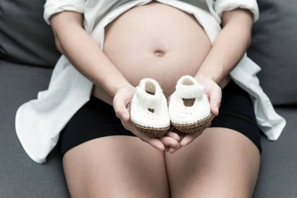 健康的中国母性观念 年轻的中国孕妇的画像在她的家和抱着婴儿鞋在她的肚子 采取室内与真正的六月大孕妇 — 图库照片