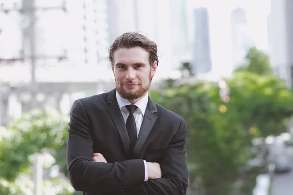 Confident young business man in black tie portrait. Handsome white male in black suit and tie, ginger hair and beard taken outdoor with natural light, confident business man concept.