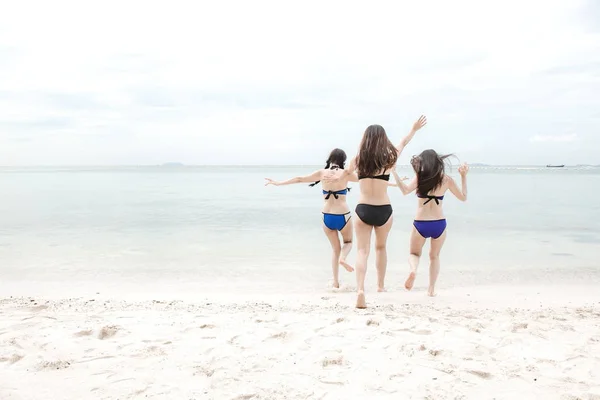 Group of beautiful young single chinese women having fun on beach. Running crazy toward the ocean, wearing bikini, beach hat.