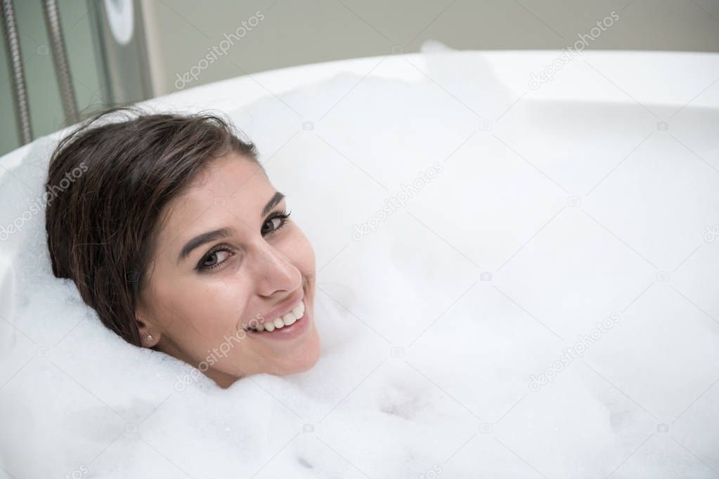 Beautiful young white woman enjoy relaxing in bubble bath. Resting, eye open, smiling. White caucasian woman.