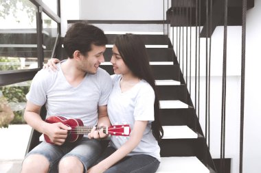 Karışık yarış severler kavramı. Banjo genç ve güzel Çinli kız arkadaşına merdivenlerde oynayan genç beyaz erkek. Giyiyor mavi jeans, mavi gömlek ve erken yirmili.