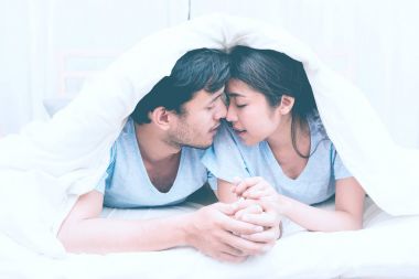 Karışık yarış severler kavramı. Battaniyenin altında oldukça genç bir Çinli kız arkadaşıyla samimi getting onun yatak odasında genç beyaz erkek. Mavi giyen kot pantolon, gömlek ve erken yirmili.