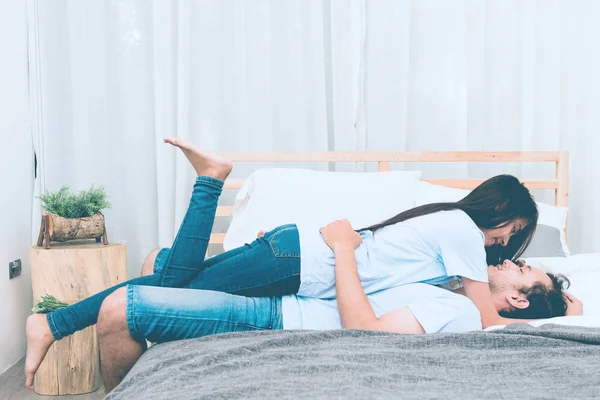 Mixed race lovers concept. Young white male in his bedroom getting intimate with his pretty young chinese girlfriend. Wearing blue jeans, blue shirt and in their early twenties. Taken indoor.