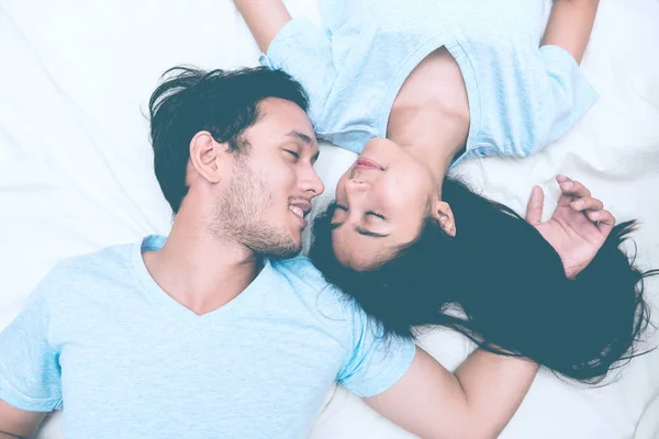 Mixed race lovers concept. Young white male in his bedroom getting intimate with his pretty young chinese girlfriend. Wearing blue jeans, blue shirt and in their early twenties. Top view.