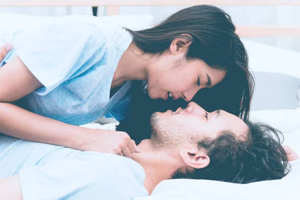 Mixed race lovers concept. Young white male in his bedroom getting intimate with his pretty young chinese girlfriend. Wearing blue jeans, blue shirt and in their early twenties. Taken indoor.