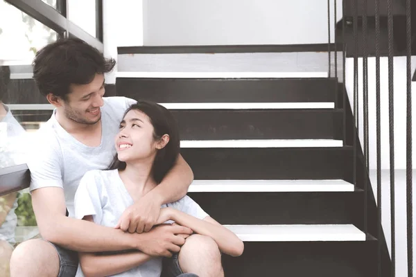 Mixed race lovers concept. Young white male hugging with his pretty young chinese girlfriend on a stairs. Wearing blue jeans, blue shirt and in their early twenties. Taken indoor.