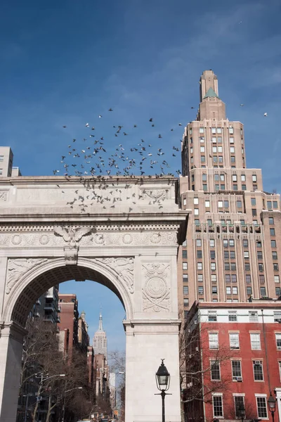 Tauben fliegen über den Bogen im Washington Square Park mit Empire State Building im Hintergrund — Stockfoto