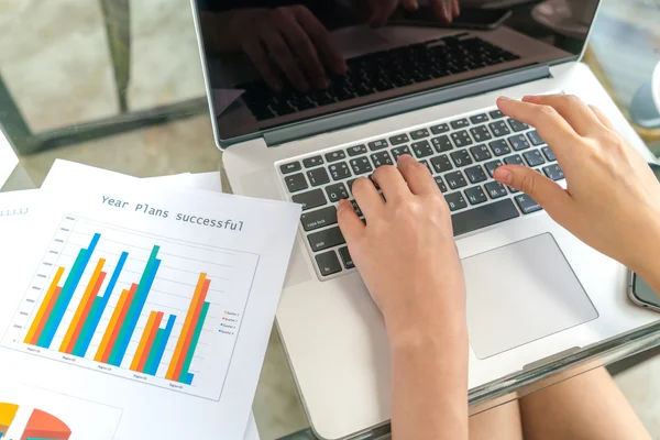 Mujer de negocios mano con gráficos financieros y portátil en la tabla — Foto de Stock