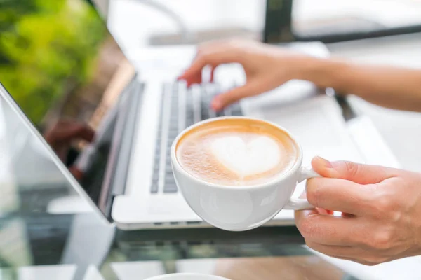 Primer plano de Latte arte café y mujer mecanografía de la mano en la clave del ordenador portátil —  Fotos de Stock