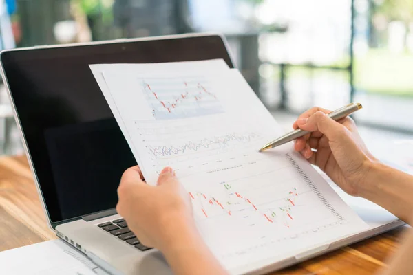 Femme d'affaires main avec des tableaux financiers et ordinateur portable sur la table — Photo