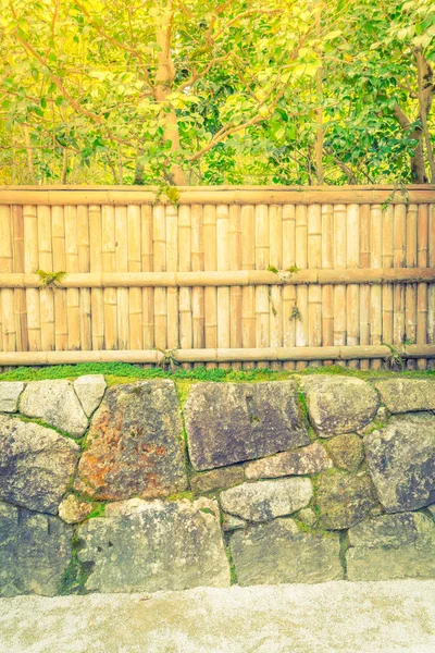 Bambusový plot na kameni se zelenými listy. (Filtrovaného obrazu proc — Stock fotografie