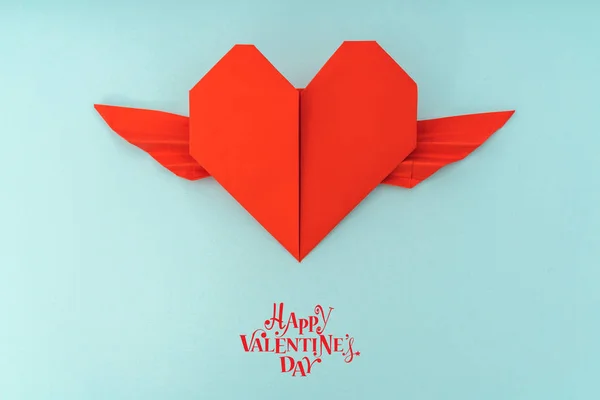 Rött papper origami hjärta med vingar på blå bakgrund . — Stockfoto