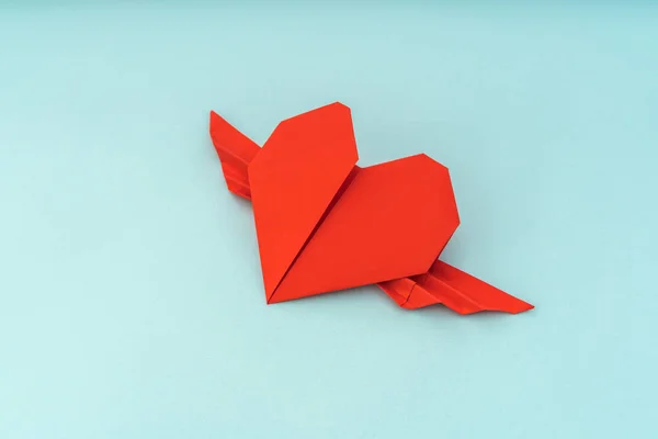 Cuore di origami di carta rossa con ali su sfondo blu  . — Foto Stock