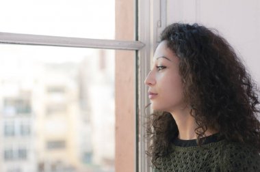 Latin woman watching through her home window clipart
