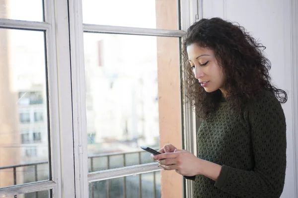 Latinsk Kvinna Chating Med Hennes Mobiltelefon Bredvid Ett Fönster Hemma — Stockfoto