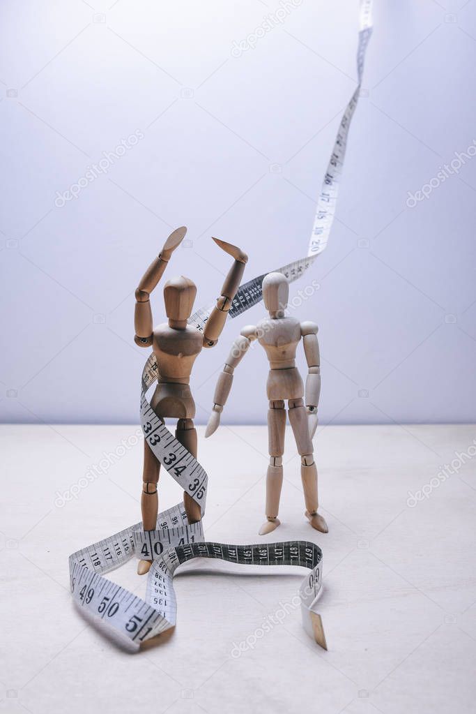 wooden mannequins with tape measure on light background