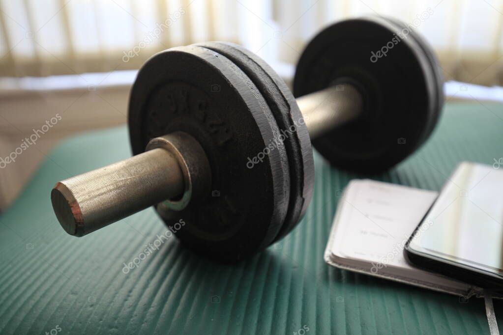 Close-up of dumbbell, notebook, pen and mobile phone.