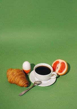 Fransız kahvaltısı sade kahve yumurtalı kruvasan ve yeşil arka planda meyve.