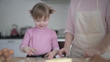 Anne ve çocuk mutfakta hamur işleri hazırlıyorlar. Aile yemekleri. Genç anne kızına yemek pişirmeyi öğretiyor. Ürünler masada. Gerçek aile hayatı. Aile akşamı. Anne ve kızı, birlikte..