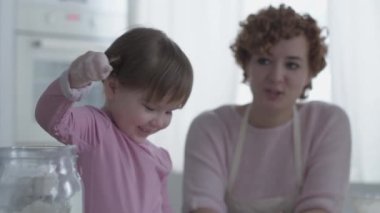 Mutfakta annesiyle yemek hazırlayan küçük bir kız. Unu at. Anne ve kızı mutfakta aşçılık oynuyorlar. Kız tatlı pişirirken yaramazdır. Birlikte oynayın.