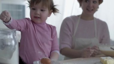 Mutfakta annesiyle yemek hazırlayan küçük bir kız. Unu at. Anne ve kızı mutfakta aşçılık oynuyorlar. Kız tatlı pişirirken yaramazdır. Birlikte oynayın.