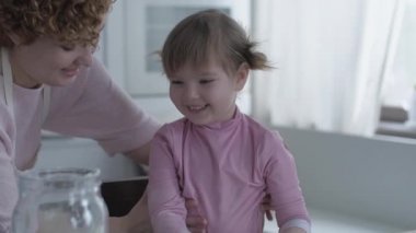 Mutfakta annesiyle yemek hazırlayan küçük bir kız. Unu at. Anne ve kızı mutfakta aşçılık oynuyorlar. Kız tatlı pişirirken yaramazdır. Birlikte oynayın.
