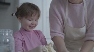 Mom teaches daughter to cook the dough. The girl learns to cook pastries. Kneading the dough together. Roll out the dough for baking. A wonderful family in the spacious kitchen prepares food. Holiday cooking sweets. Little helper in the kitchen.