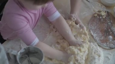 Mom teaches daughter to cook the dough. The girl learns to cook pastries. Kneading the dough together. Roll out the dough for baking. A wonderful family in the spacious kitchen prepares food. Holiday cooking sweets. Little helper in the kitchen.